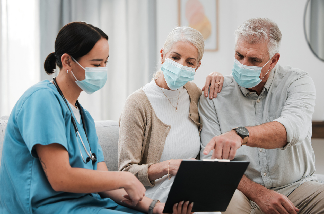 Masked senior couple with healthcare nurse looking at a clipboard