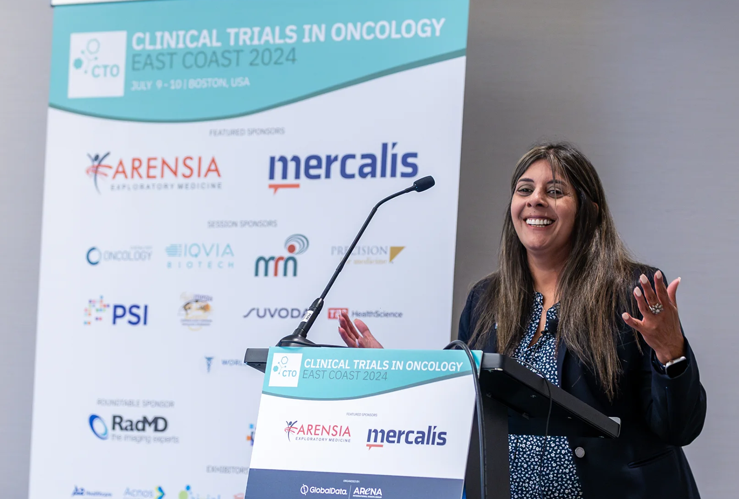 A smiling Keya Watkins gesturing at a podium at Clinical Trials in Oncology.