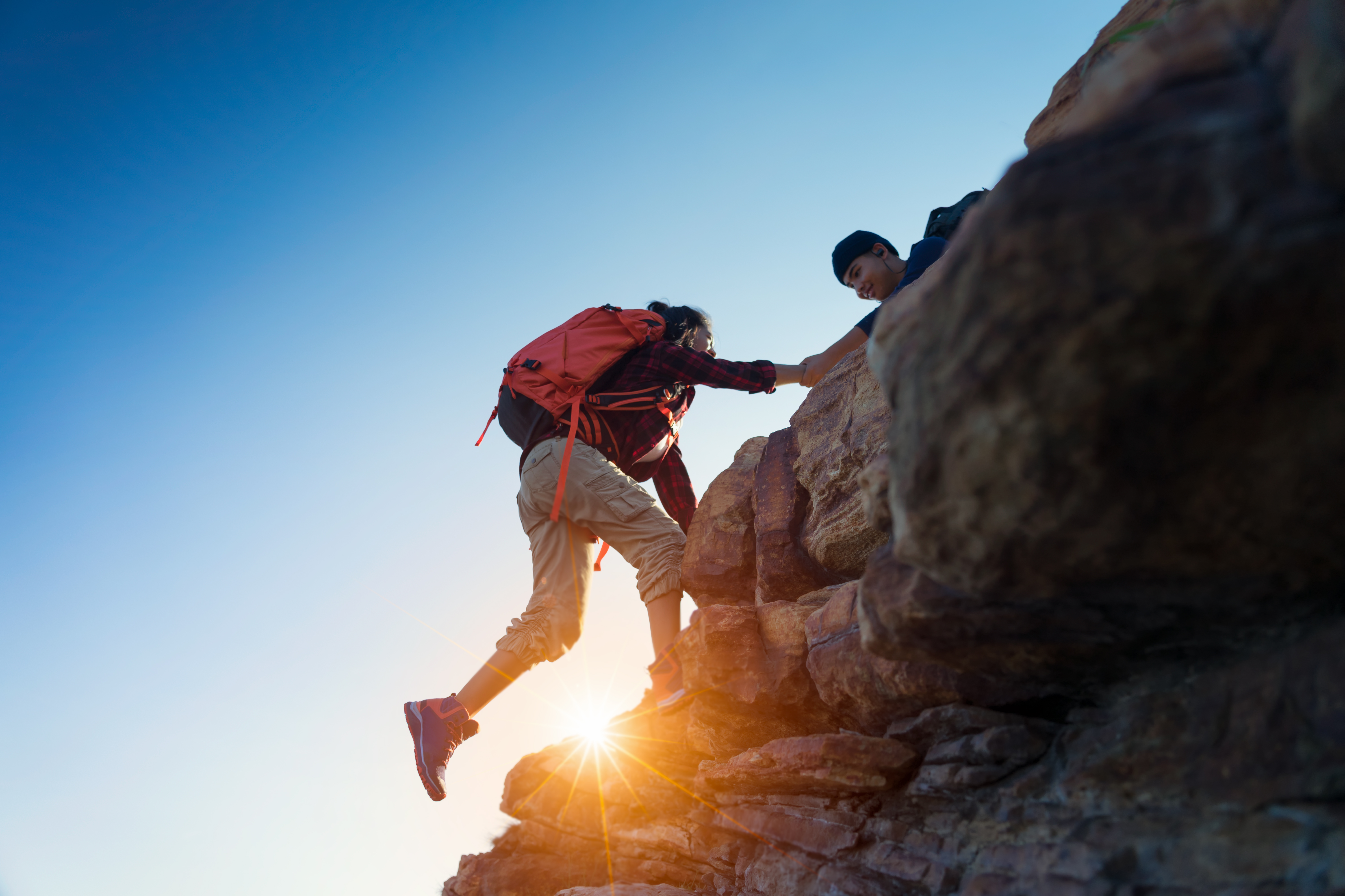 A hiker lending a hand to another with the sun in the background