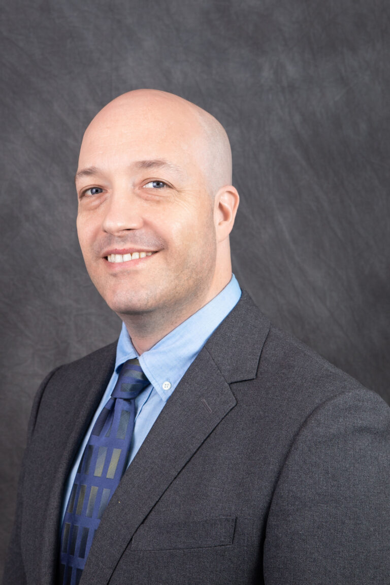 Photo of Michael Caskey smiling and wearing a suit and tie.