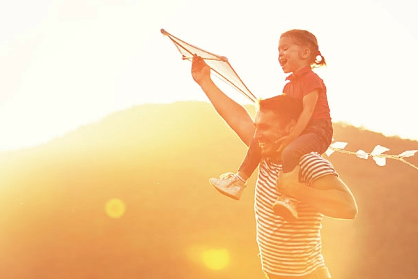 Child on man's shoulders who is holding a kite with lots of sunshine