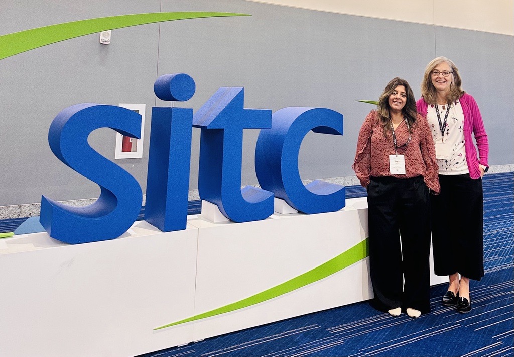 Photo of Keya Watkins and Sue Albert at the SITC sign during the SITC conference.