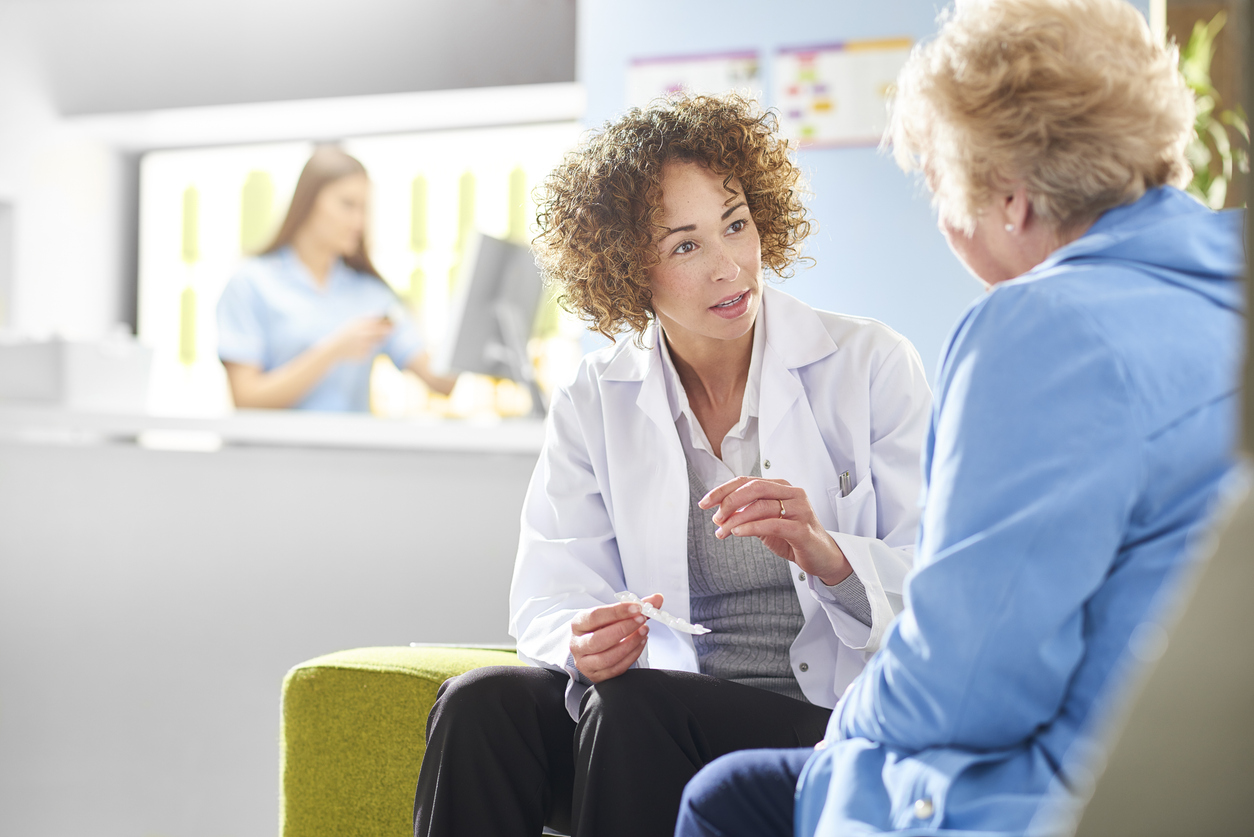 A female medical professional sits with a senior female patient.